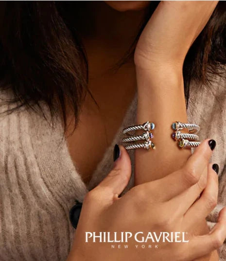 A woman elegantly showcases Phillip Gavriel jewelry, featuring intricate designs in gold and silver, accented with vibrant gemstones.